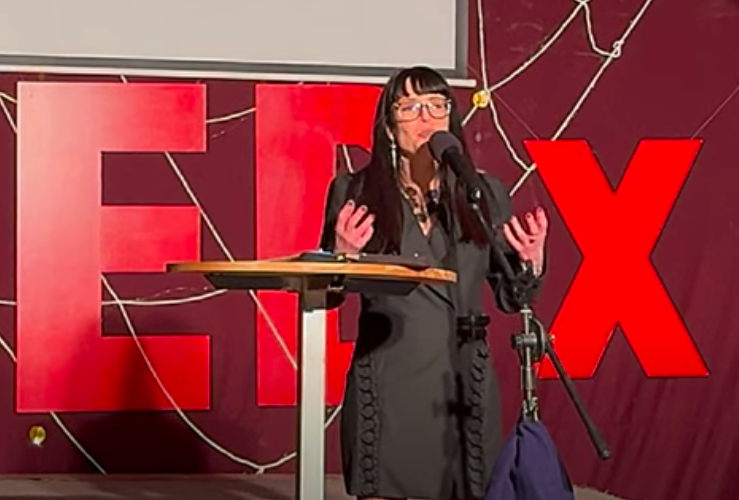 Lauren Muratore is on stage with tedx logo behind her and microphone in front of her.